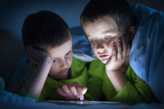 boys playing on a tablet computer electronic device in bed