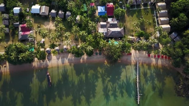 Looking straight down onto an island village with palapas, grass roofs and beach, the camera moves out over the clear water of this island paradise.