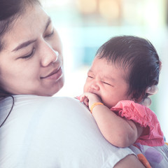 Cute asian newborn baby girl crying with tried on mother's shoulder.Young mother cuddling baby with tenderness.