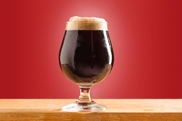 glass of cold frothy dark beer on an old wooden table