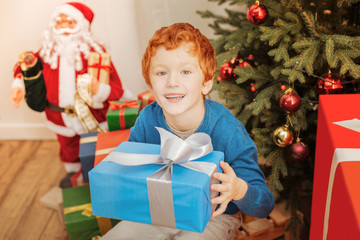 Obraz na płótnie Canvas Excited redhead kid smiling while holding his christmas present