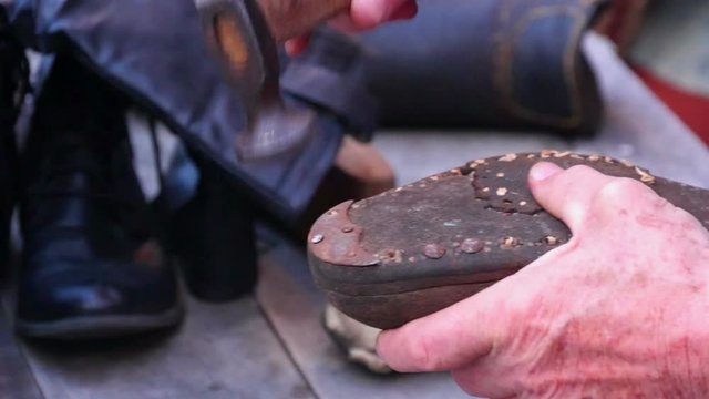 Old shoemaker showing old handscrafts repairing vintage shoes. Hammering steel nails in shoes sole. Shot in slow-motion hd.