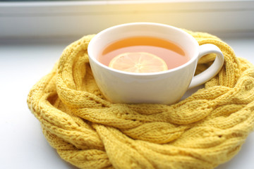 Mug of hot tea in a scarf on a window sill at a window