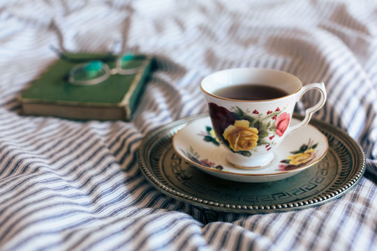 Fototapeta Black tea in china cup on vintage tray with closed book and glasses