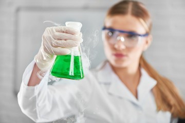 Selective focus on a flask with green smoking chemical liquid in the hand of a young female researcher at the laboratory copyspace profession occupation education medicine development concept.