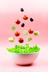 Tofu cheese, cherry tomatoes and olives flying out of the white bowl on a pink background. Concept of a healthy diet. Selective focus