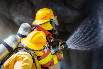 Naklejka premium two firefighters water spray by high pressure nozzle to fire surround with smoke and copy space