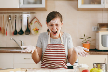 A young perplexed and confused woman sitting at a table with flour and going to prepare a Christmas...