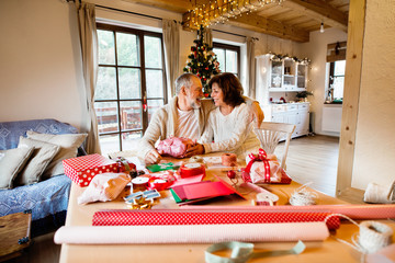 Senior couple in sweaters wrapping Christmas gifts together.