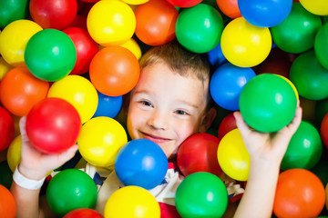 Fototapeta na wymiar Small boy in a pit full of colorful plastic balls