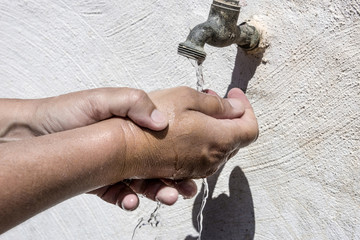 One hand washes the other - concept with two hands in running water and an old tap on a white wall