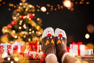 Foto auf Acrylglas Detail of woman legs with knitted socks, Christmas tree with gifts on background © Jag_cz
