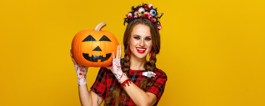 smiling young woman showing jack-o-lantern pumpkin