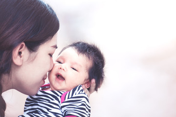 Young asian mother hugging and kissing her newborn baby girl with love in vintage color tone