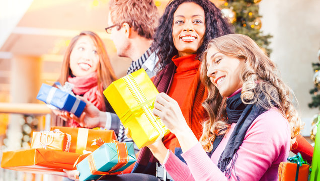 Leute verschiedener Hautfarbe sitzen mit Weihnachtsgeschenken und Tüten in einem Einkaufszentrum oder einem Kaufhaus vor einem Weihnachtsbaum mit Kugeln