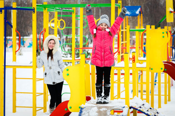 Two happy girls, mother and daughter  playing on a  playground at winter frosty day.