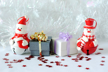 des bohomme de neige posés à coté des cadeaux avex noeuds brillants sur un décor de fêtes de Noël