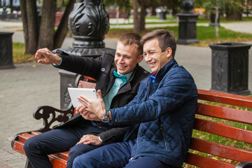 two guys in business style clothes on a park bench. Information exchange. Businessmen with gadgets