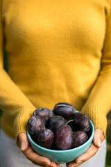 Adult woman holds a bowl of plums in her hands