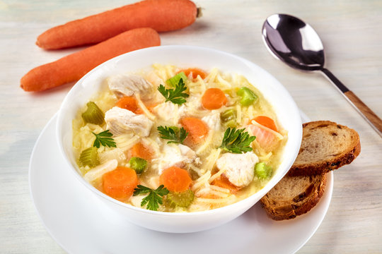 Closeup of chicken soup with noodles, bread, and carrots
