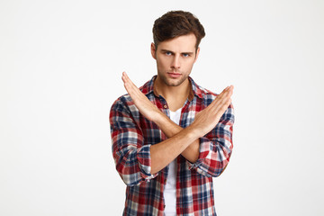 Close-up photo of serious handsome young man showing stop gesture with crossed hands, looking at...