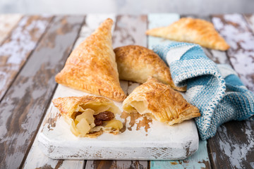 Puff pastry triangles filled with apples, dutch appelflappen on old cutting board. Homemade food...