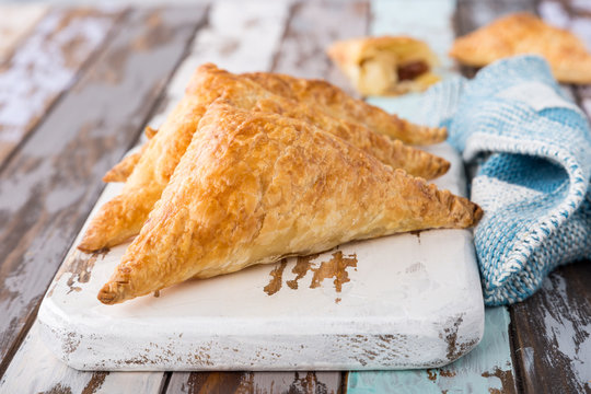 Puff pastry triangles filled with apples, dutch appelflappen on old cutting board. Homemade food concept, close up.