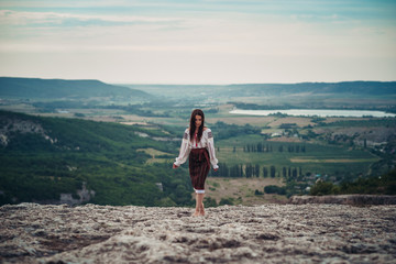 Naklejka na ściany i meble Atractive woman in traditional romanian costume on mountain green blurred background. Outdoor photo. Traditions and cultural diversity