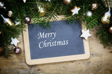 Slate writing board with fir tree branches, christmas balls and cookies on a rustic wooden board, sample text Merry Christmas