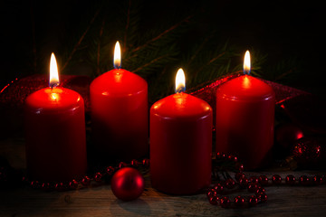 Four red burning candles at the fourth advent, christmas decoration with spruce twigs and baubles on a rustic board, dark background