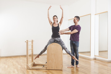 Pilates lesson on barrel, personal trainer coaching young beautiful woman