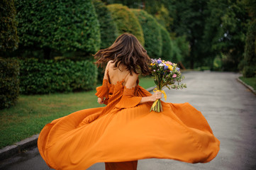 Obraz premium Back view of attractive woman in long orange dress