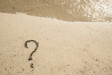 Question mark sign on sand beach near the sea and waves