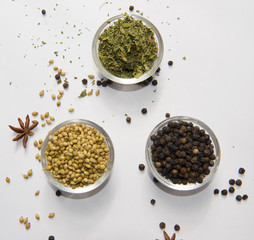 Coriander seeds, black pepper, and dried fenugreek leaves in glass bowls. Essential spices for Indian and global cuisine, adding citrusy, bold, and aromatic flavors. A rustic display of natural herbs