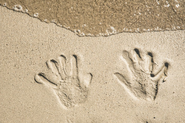 A trace of hands on the wet sand near the sea and waves