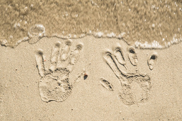 A trace of hands on the wet sand near the sea and waves