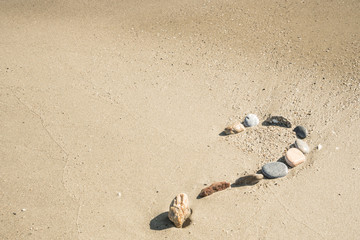 Fototapeta na wymiar Question mark sign made of different shells on sand beach near the sea and waves