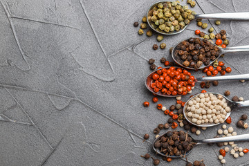 Black (cubeb), pink and white pepper in spoon on black table. Multicolored spice closeup. Selective focus. Top view, copy space