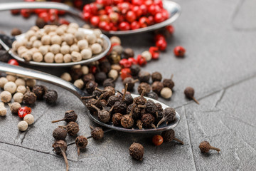 Black (cubeb), pink and white pepper in spoon on black table. Multicolored spice closeup. Selective focus