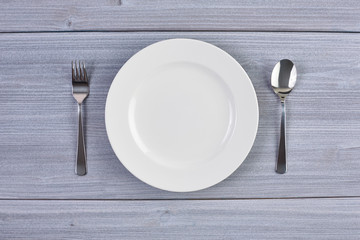Top view of white dish with fork and spoon on background of wooden table