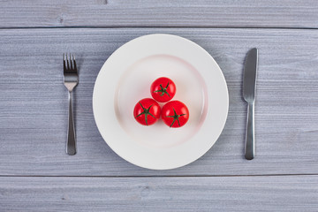 Top view of white dish with tomato on background of wooden table