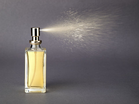 Bottle of golden colored perfume with spray jet on gray background