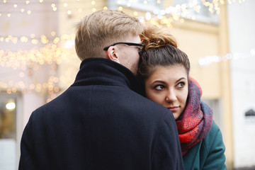 Fototapeta premium Interracial cute young couple embracing on street decorated with sparkling garland colorful lights. People, relationships, togetherness, love, holiday, Christmas, New Year and happiness concept