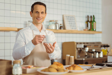 Delighted positive man holding a cup of coffee