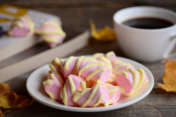 Light pink and yellow marshmallow on a plate, a cup of coffee, books, yellow autumn leaves on a vintage wooden table. Nice autumn reading concept