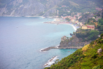 Fototapeta premium Aerial view to the beach and coastline of Monterosso al Mare, Cinque Terre, Italy. Houses, parked cars and beautiful green mountains.