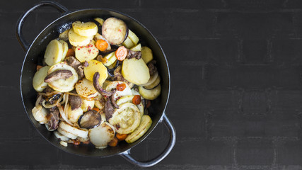 Slow cooked vegetables and beef stew in cast iron pot, top view. Copy space.