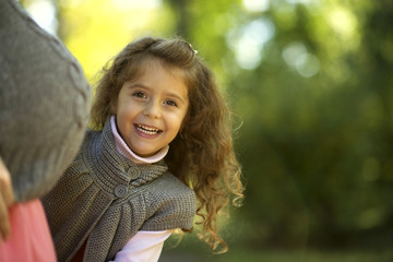 curly-haired girl in an autumn park looks out for mother's pregnant belly