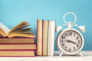 Vintage alarm clock and pile of books on against a blue background. Concept of education.