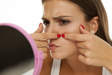 young woman looking at herself in the mirror and squeezing pimples